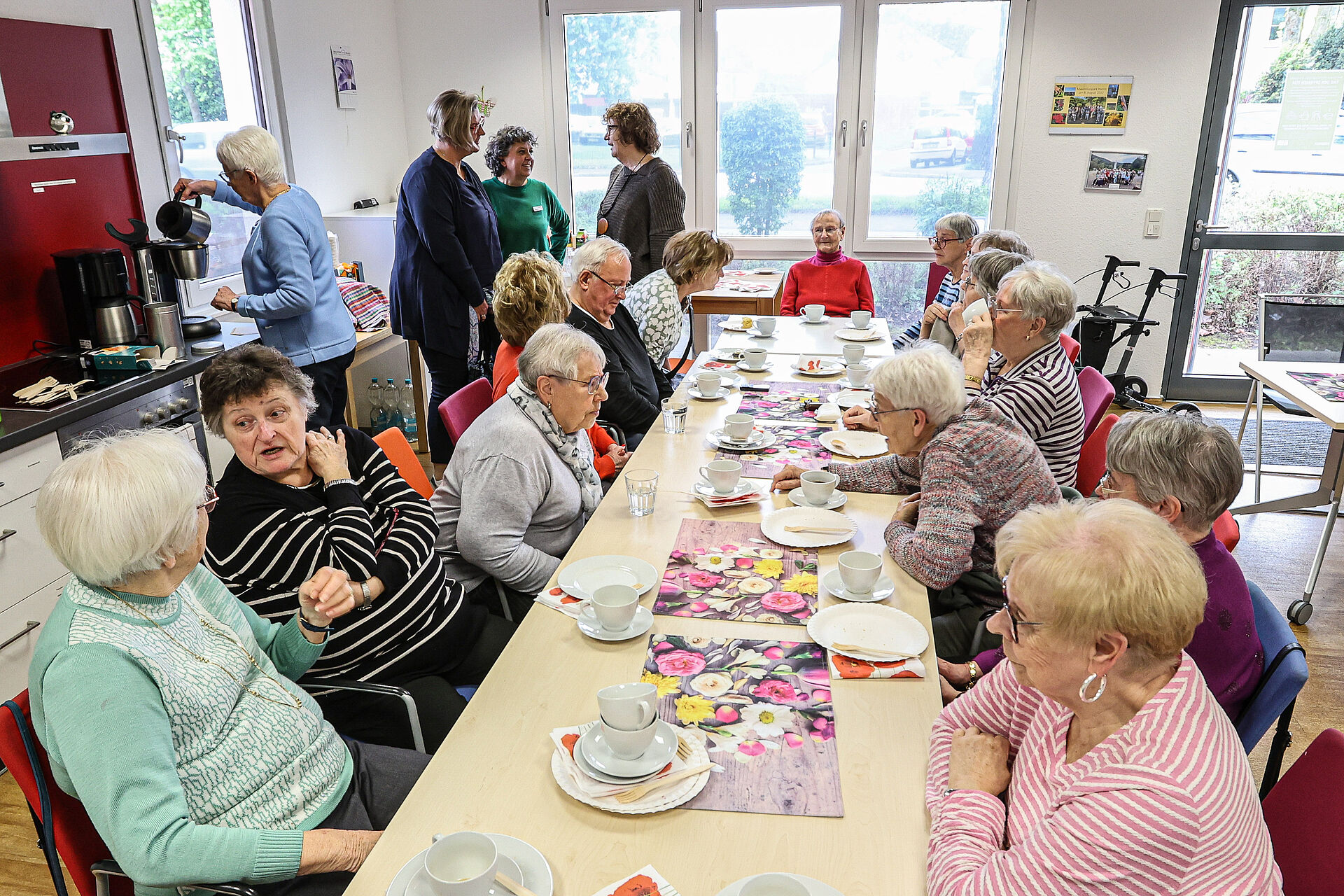 Einige Frauen und Männer im Seniorenalter sitzen an einer schön gedeckten Tafel bei Kaffee und Kuchen in einem hellen Raum der Nachbarschaftsagentur in Mengede