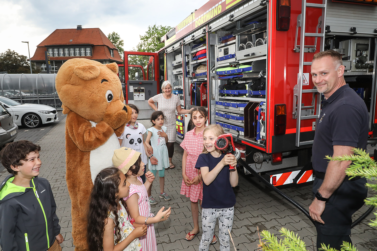 Kinder bekommen zusammen mit dem Dogibär von der Feuerwehr den Einsatzwagen gezeigt.