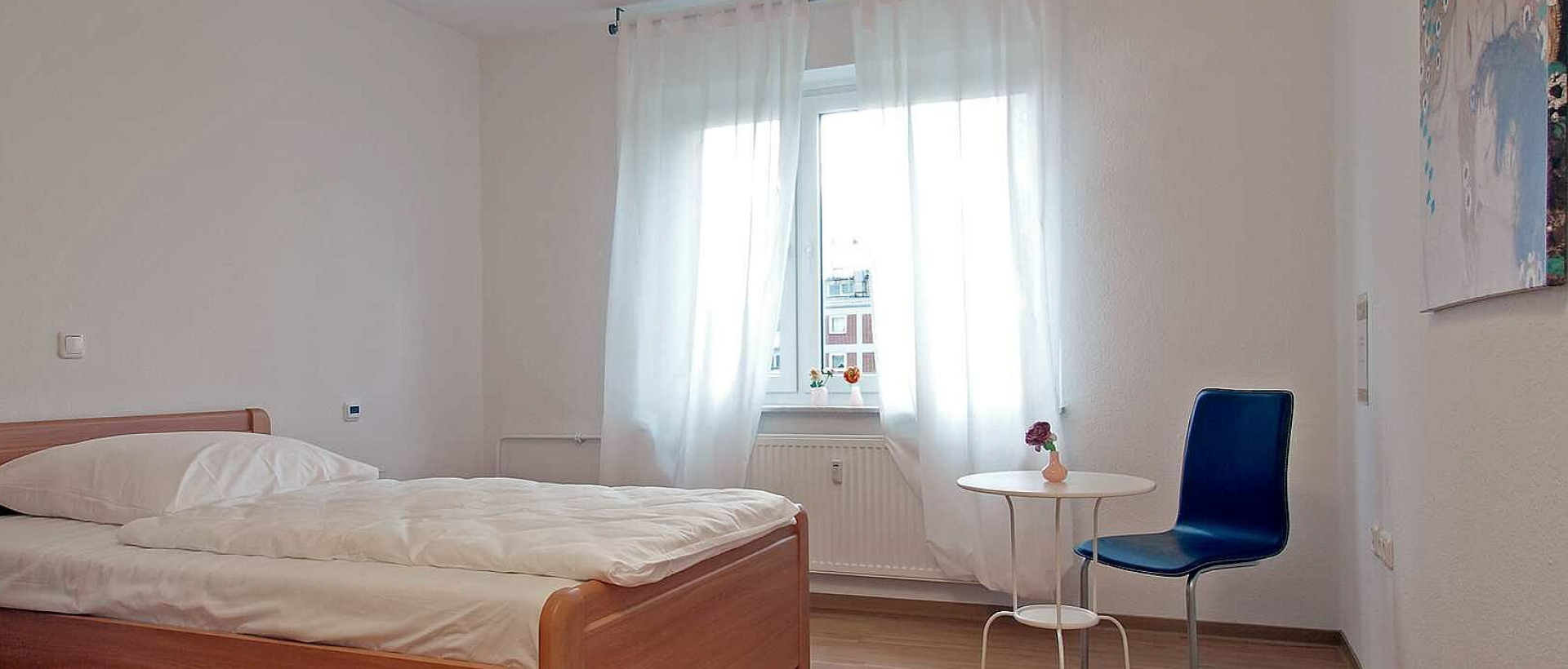 Ein Bett mit weißer Bettdecke steht in einem weißen Zimmer mit blauem Sessel