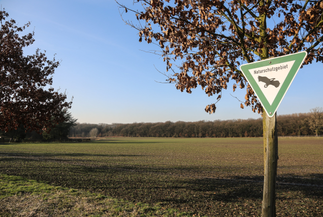 Ein offenes Feld mit einem Naturschutzschild im Vordergrund