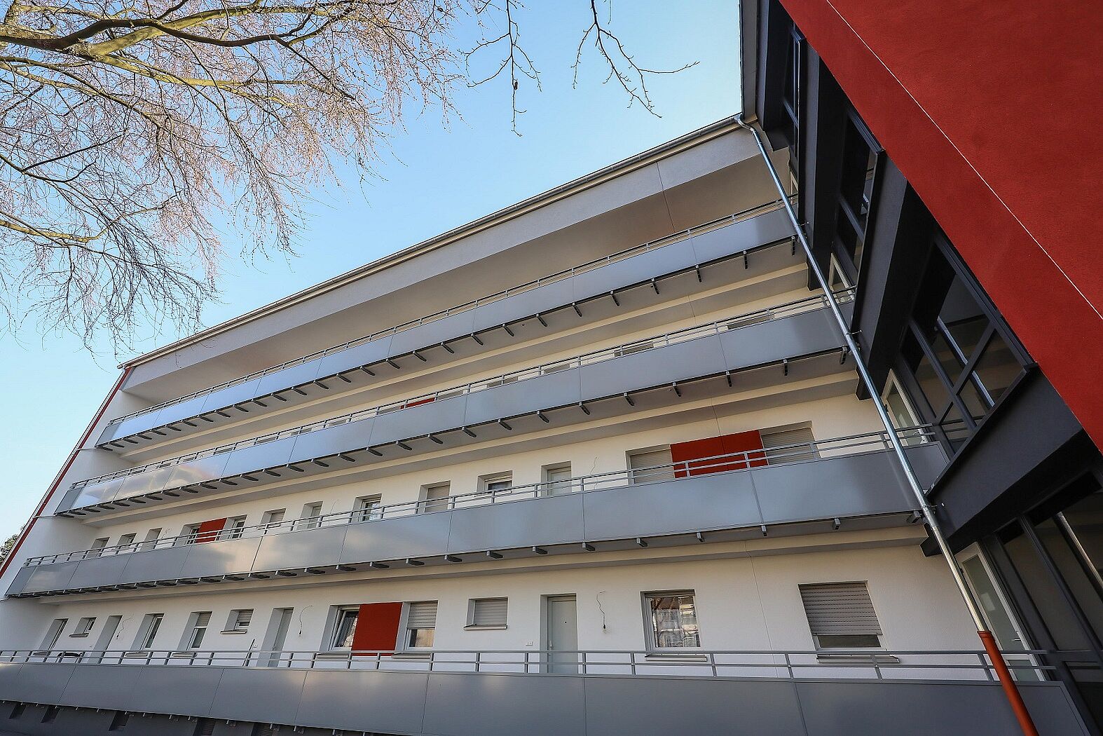 Energetisch modernisiertes Mehrfamilienhaus mit Laubengängen und neuen Treppenhäusern in rot und antrazithfarben.