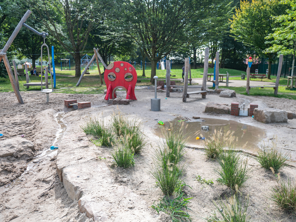 Wasserspielplatz mit Spielmöglichkeiten und ein Beet mit Gräsern