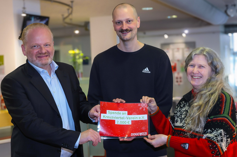 Drei lächelnde Menschen stehen im Foyer von DOGEWO21 und halten einen symbolischen Spendenscheck in den Händen.