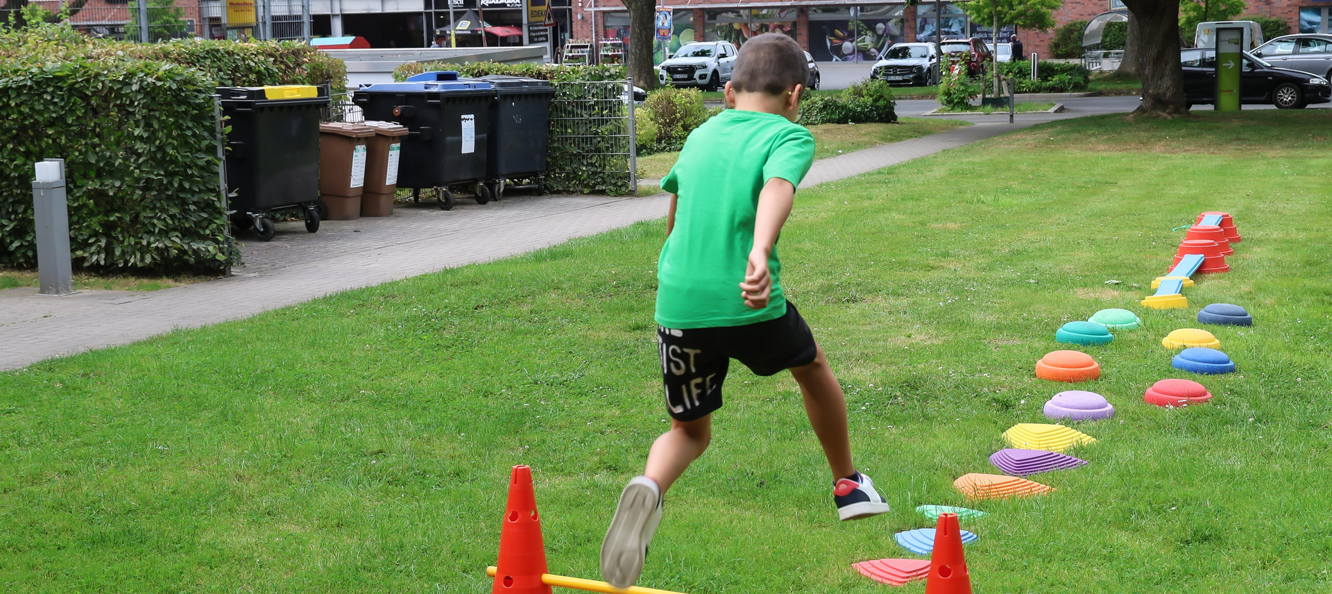 Kind springt über einen Hindernisparcours auf einer grünen Wiese.
