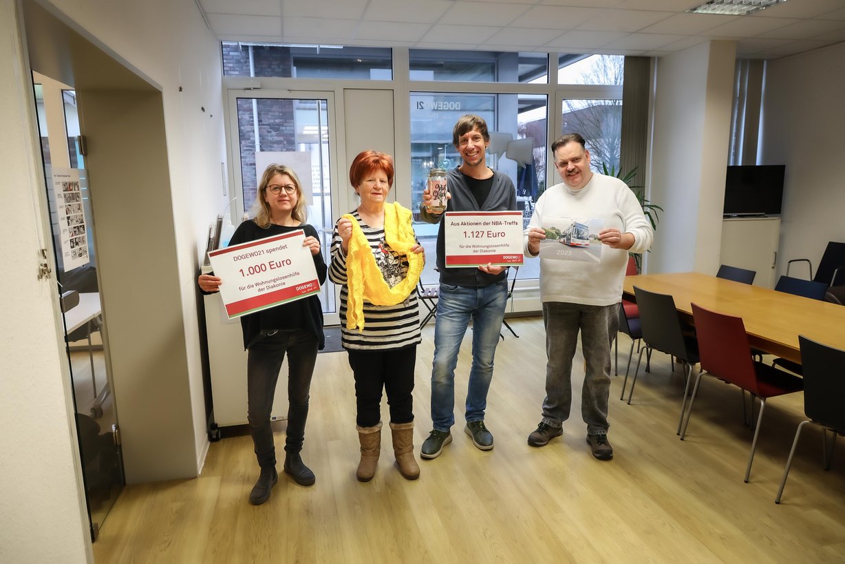 Menschen bei der Übergabe von zwei symbolischen Spendenschecks in einer DOGEWO21-Nachbarschaftsagentur