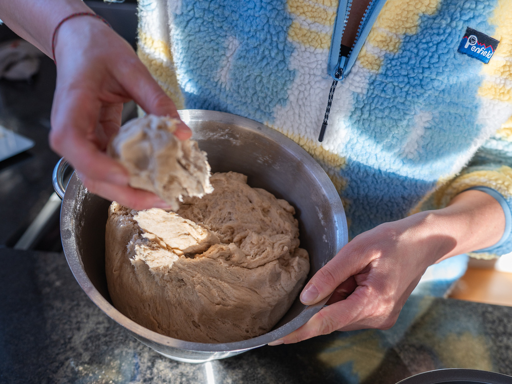 Ein Teigballen in einer Schüssel und ein kleines Stück Teig in einer Hand.