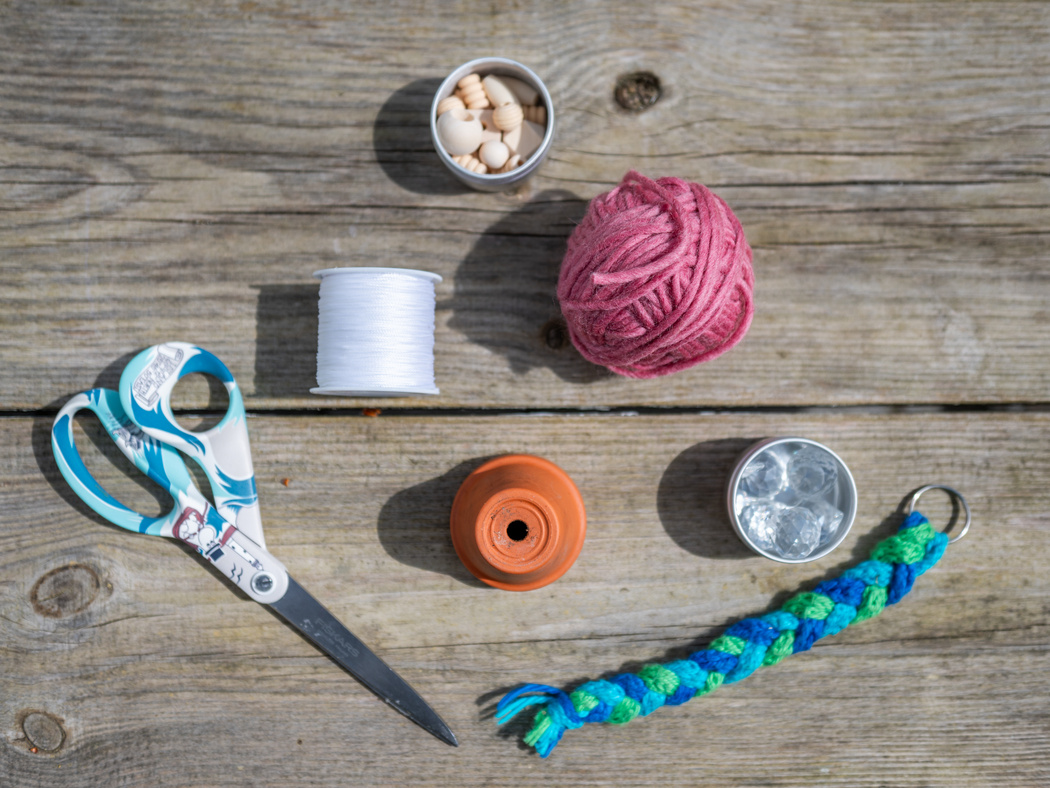 Eine Schere, ein Tintopf, Perlen, Kristallperlen, eine Schnur und ein Schlüsselanhänger aus geflochtener Wolle auf einem Holztisch