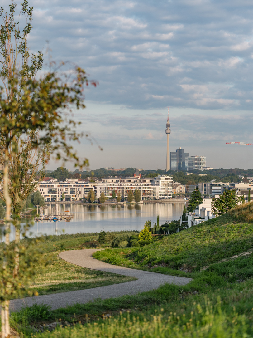 Spazierweg an einem See mit Blick auf Häuser an der Promenade.