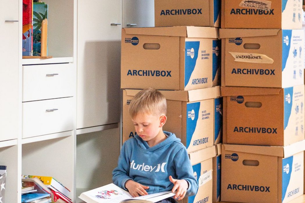 Junge liest ein Buch und lehnt sich an Umzugskartons