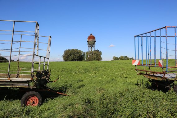 2 leere Heuwagen auf einer Wiese und einem Wasserturm im Hintergrund