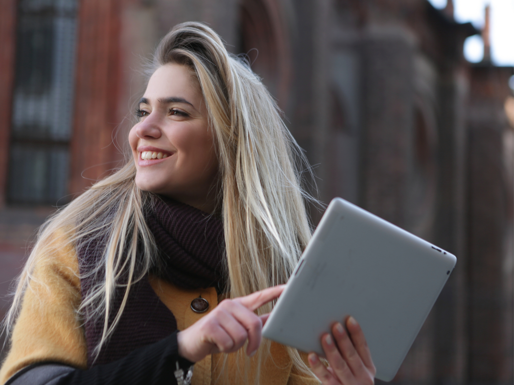Eine lächelnde Frau, die ein Tablet in der Hand hält.