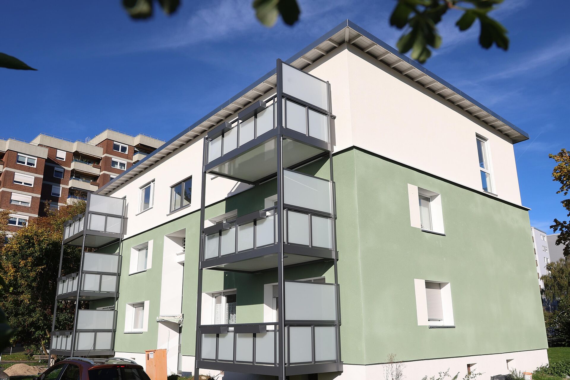 Grün-weißes Mehrfamilienhaus mit aufgestockten Dachgeschosswohnungen und neuen Anstellbalkonen