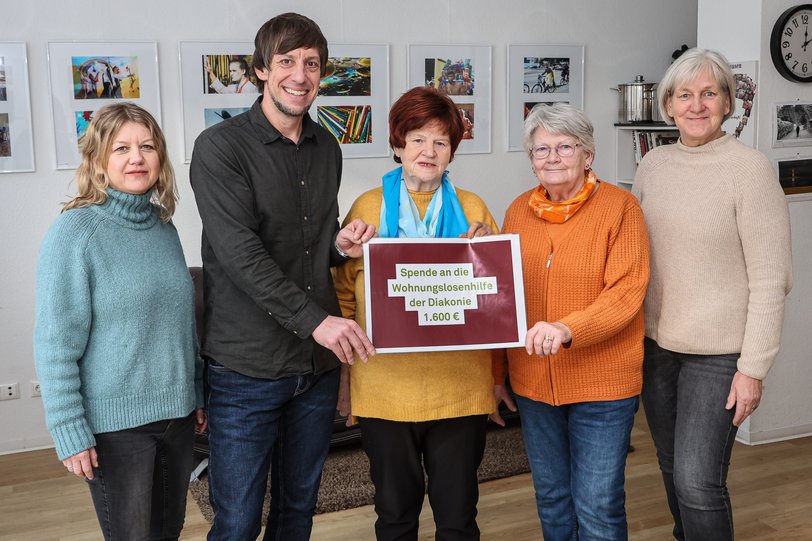 Fünf Menschen stehen in einem Raum der Nachbarschaftsagentur und halten einen symbolischen Spendenscheck in Richtung Kamera.