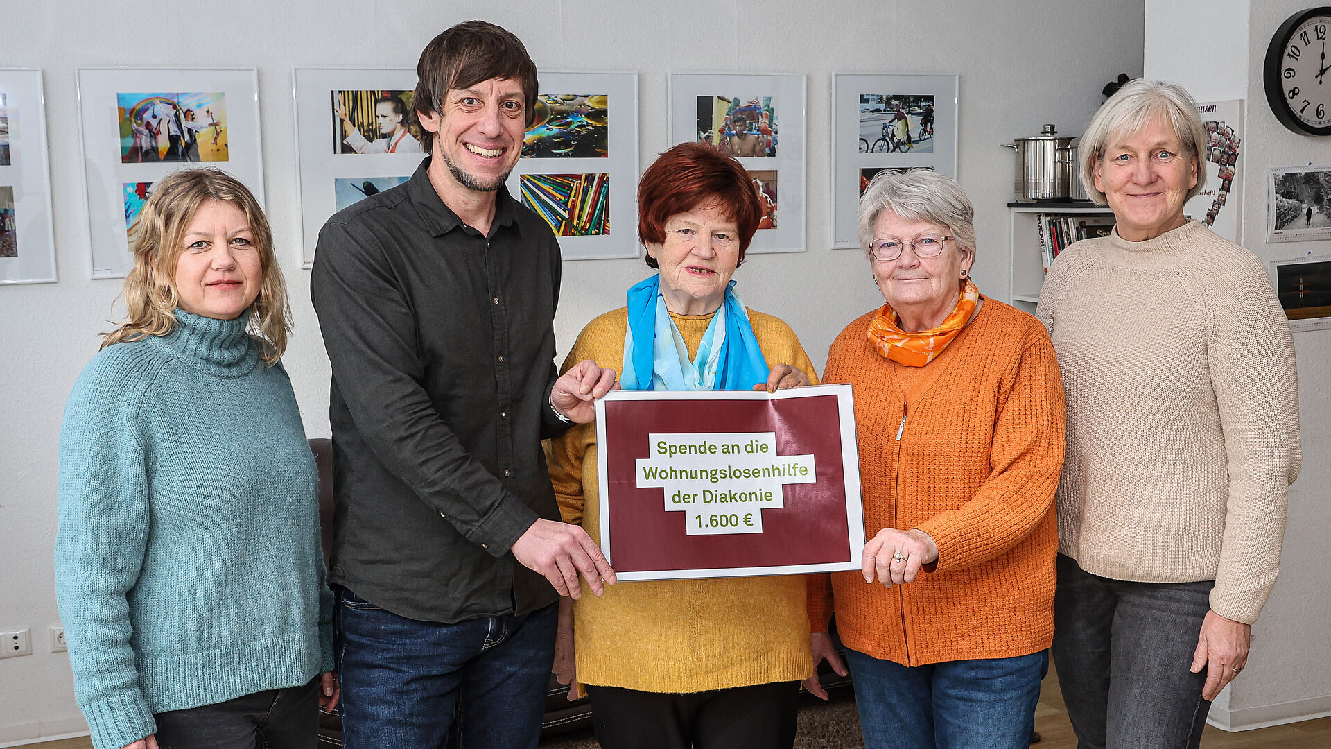 Fünf Menschen stehen in einem Raum der Nachbarschaftsagentur und halten einen symbolischen Spendenscheck in Richtung Kamera.