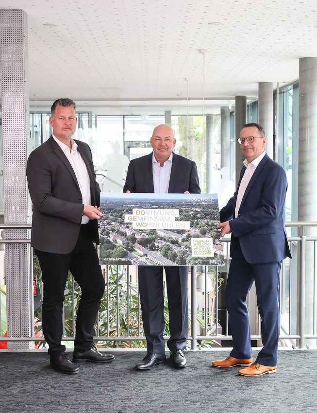 Die drei Herren der Geschäftsleitung von DOGEWO21 präsentieren ein Plakat mit QR-Code und dem Bild des digitalen Geschäftsberichts 2023.