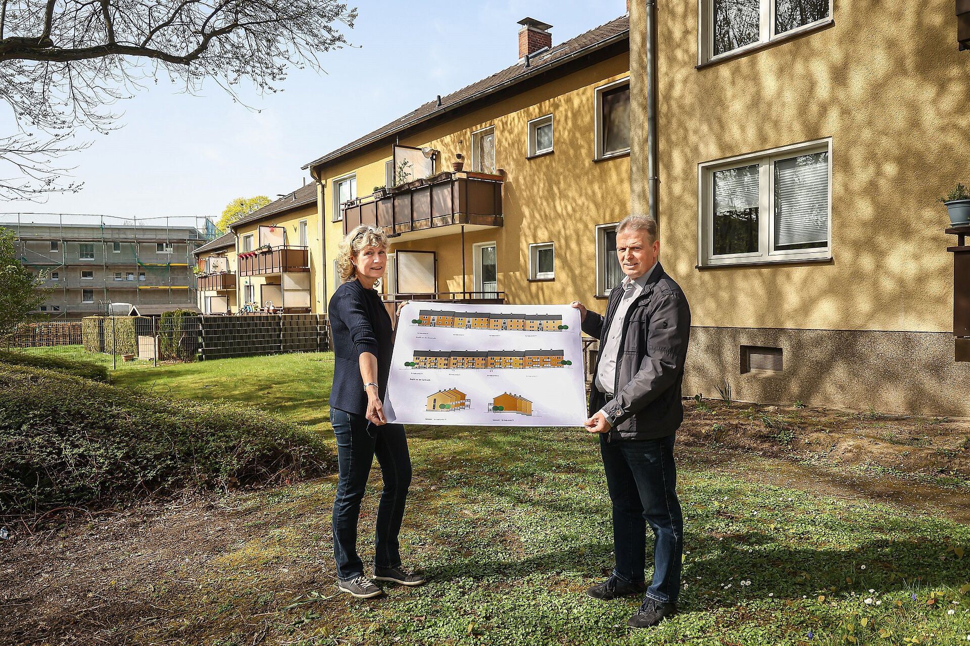 Zwei Mitarbeitende von DOGEWO21 halten einen Plan hoch, der die Modernisierungsmaßnahmen von Mehrfamilienhäusern zeigt