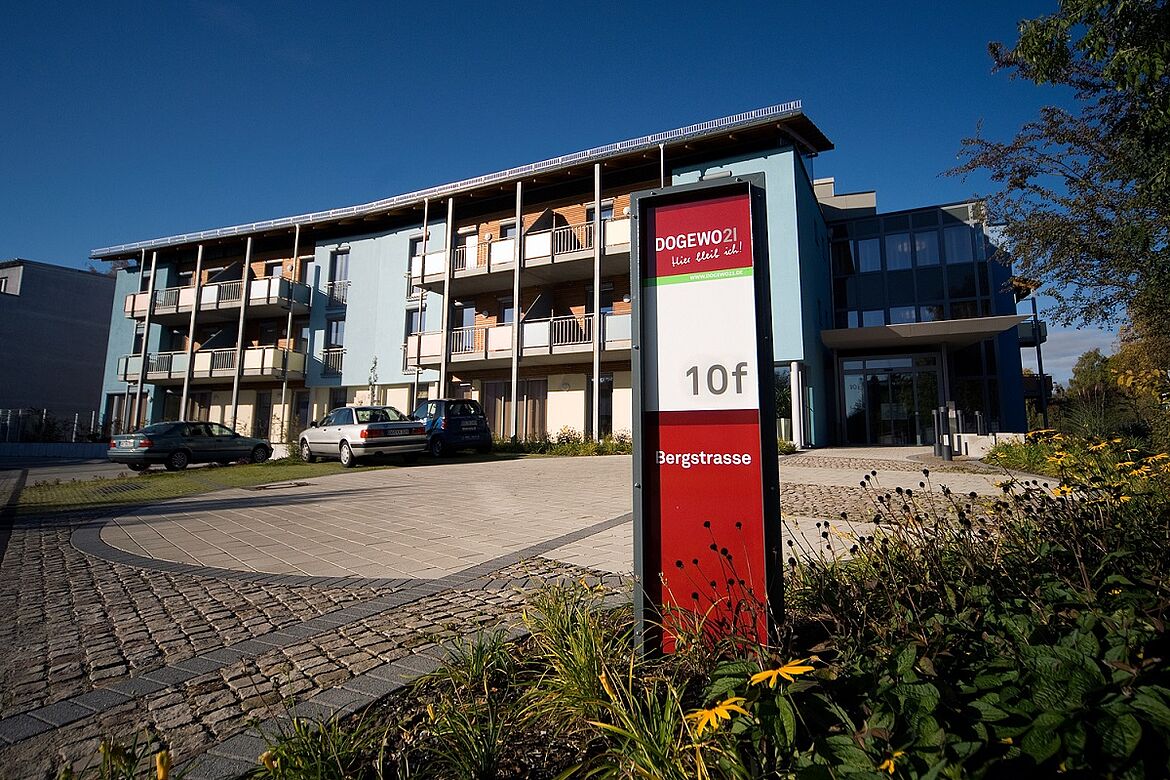 Frontansicht des blau gestrichenen Seniorenwohnhauses Sonnenhof mit Grünflächen und Parkplätzen vor dem Haus.