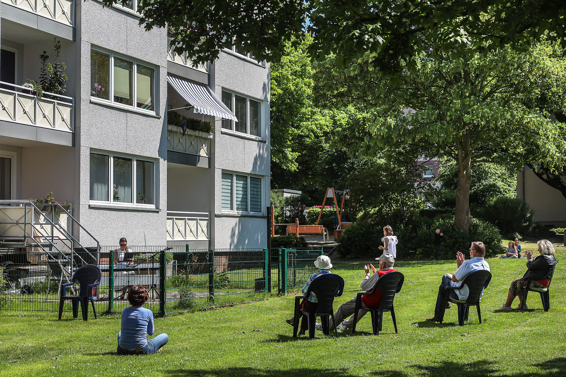 Bewohner sitzen im Garten und schauen einer Klavierspielerin zu