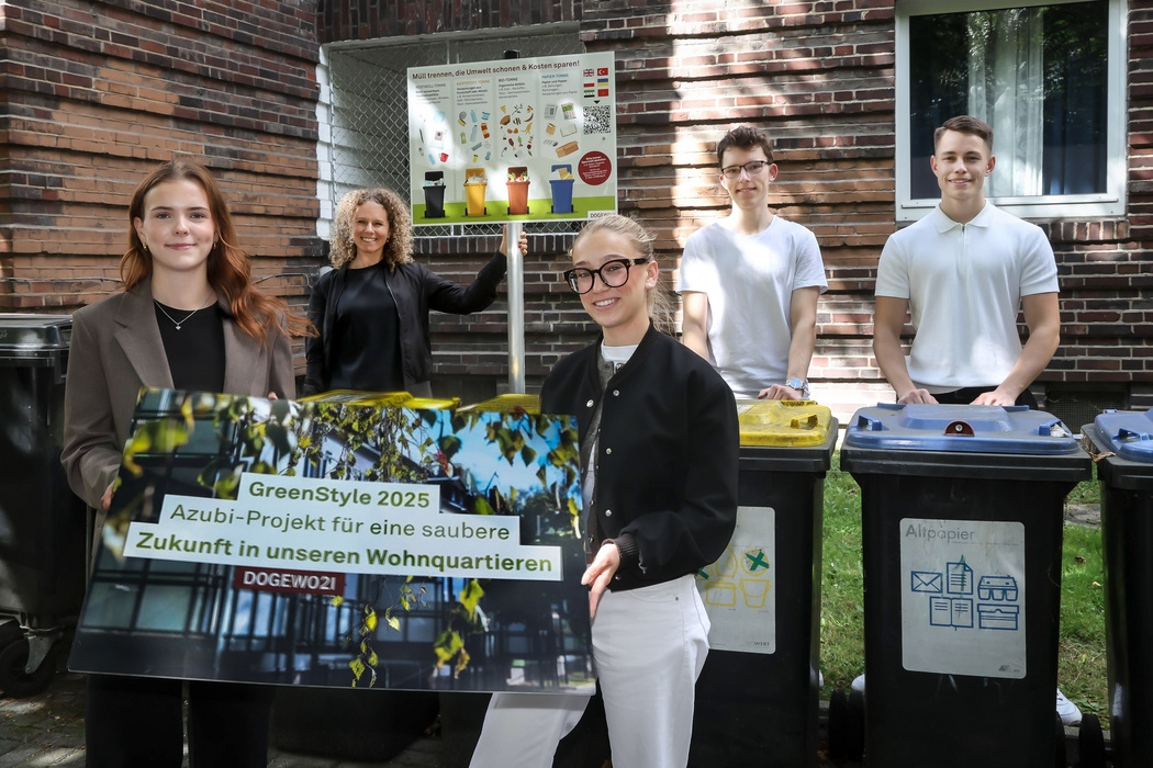 Die DOGEWO21 Azubis stehen von einem Müllstandplatz, an dem ein neues Schild mit Hinweisen zur Mülltrennung montiert wurde.