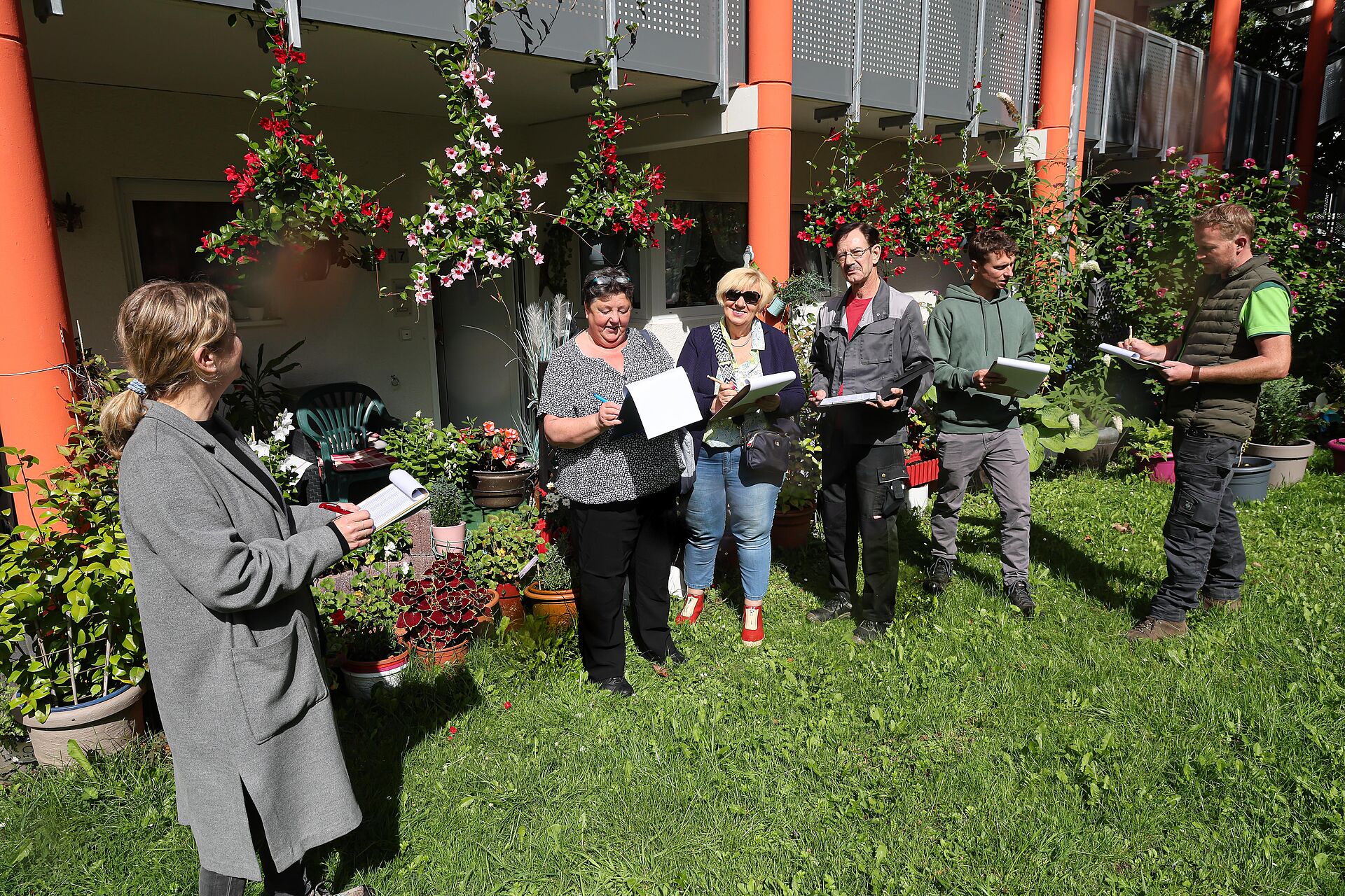 Eine Jury aus mehreren Menschen bewertet die üppige Blütenpracht der bepflanzten Terrassentöpfe in einem Wohnhaus