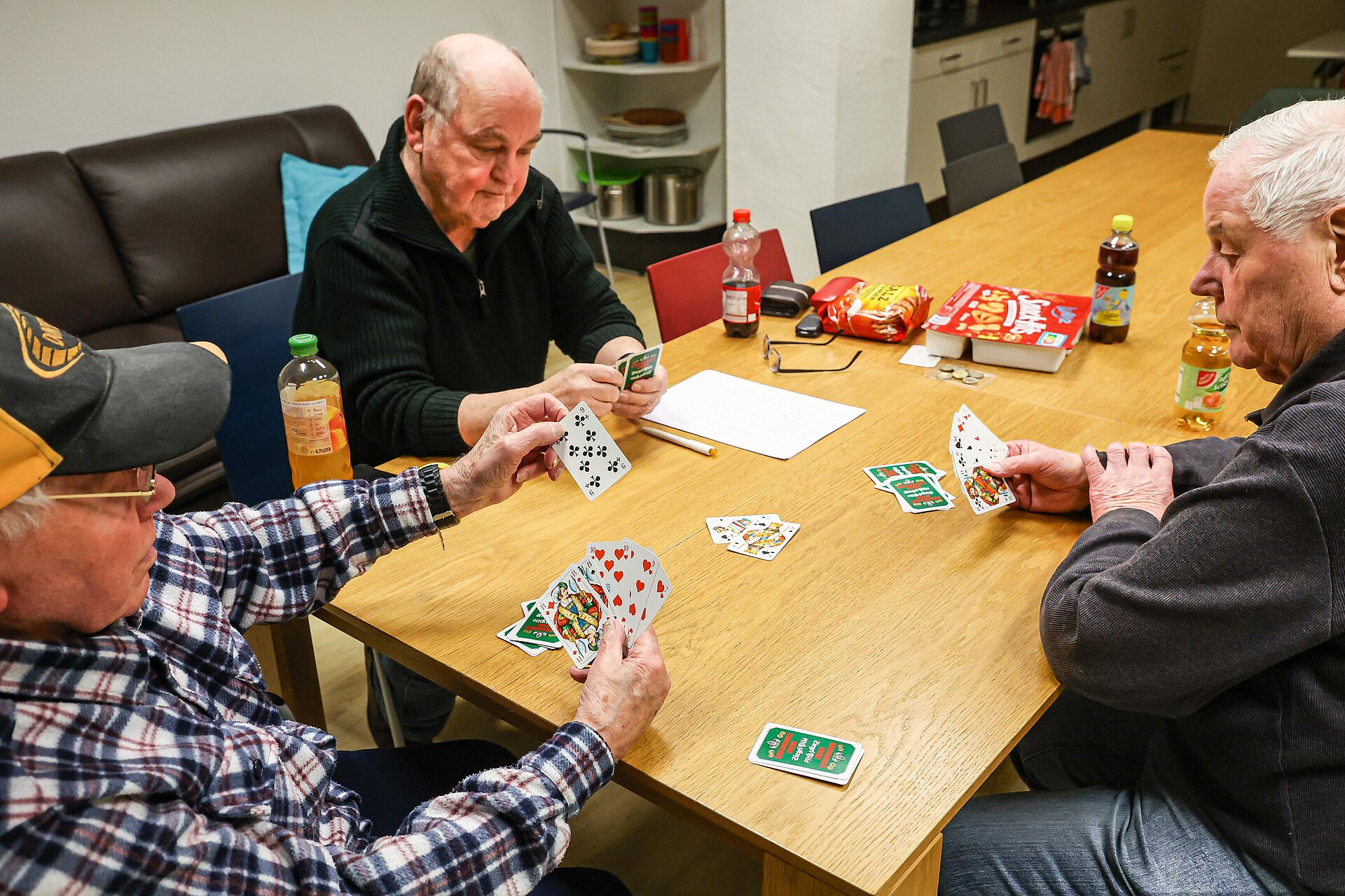 Drei Männer sitzen an einem Tisch und spielen Skat