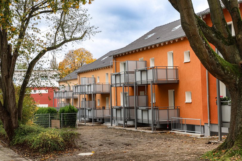 Blick durch den Garten auf orangefarbene Mehrfamilienhäuser mit großen, angestellten Balkonen