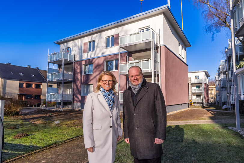 Eine Frau und ein Mann stehen vor einem energetisch modernisierten Haus, dessen Dach durch Aufstockung zwei neue Wohnungen bekommen hat.