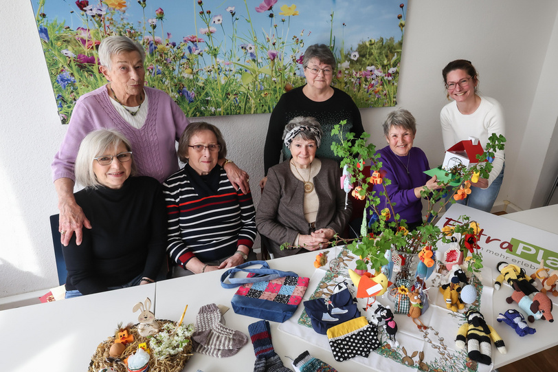 Mehrere Frauen überreichen an einem mit Handarbeiten und Blumen dekorierten Tisch eine Spende. 