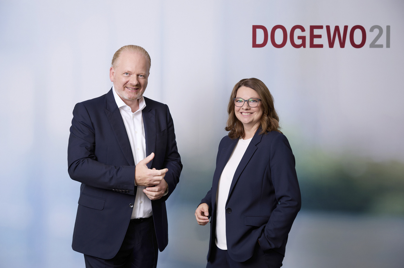 Samuel Serifi und Sabrina Rahne stehen vor einer Logowand und lächeln.