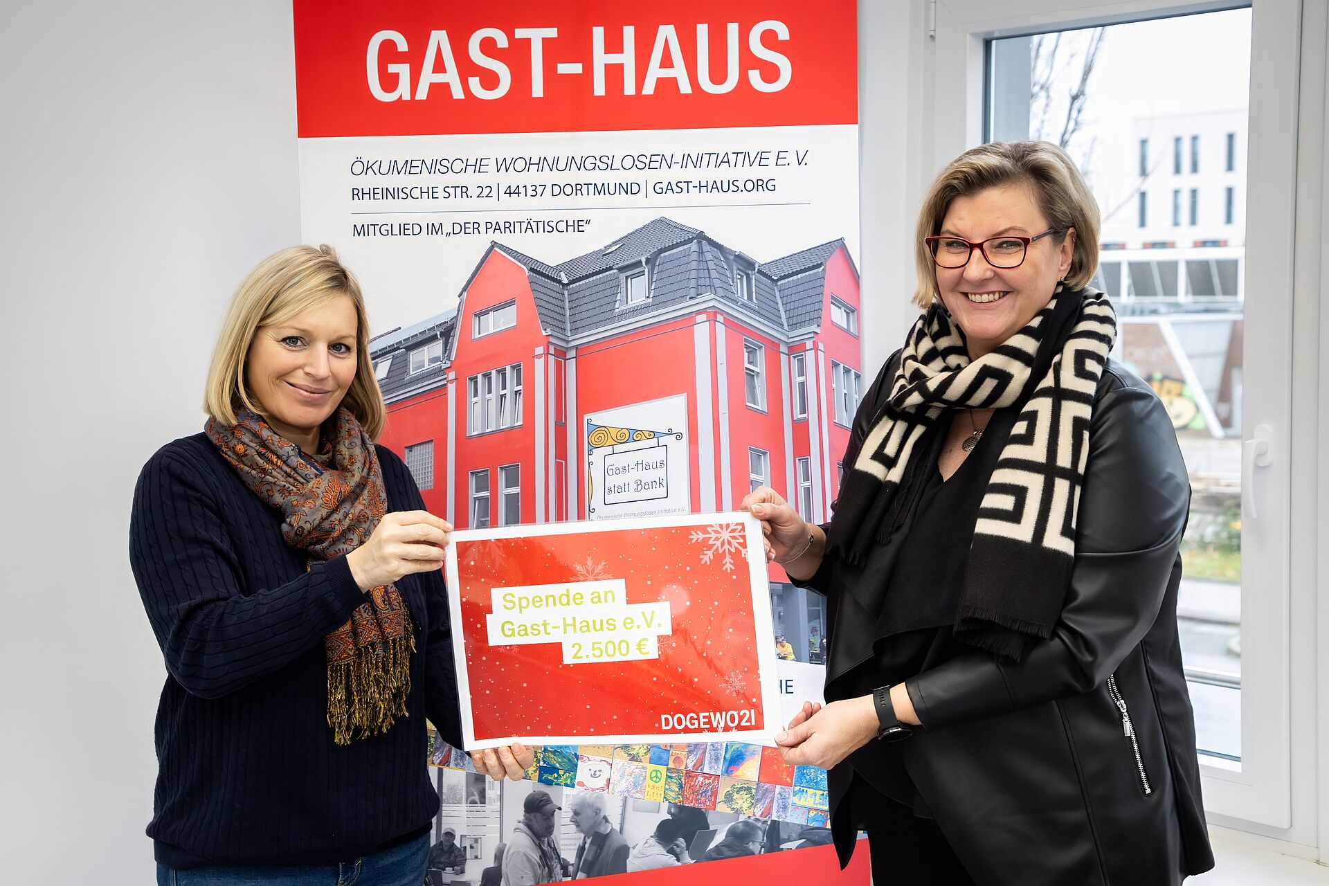 Zwei Frauen stehen bei der Übergabe eines symbolischen Spendenschecks in den Räumlichkeiten der Wohnungslosen-Initiative Gast-Haus 