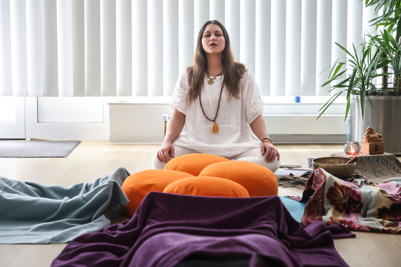 Eine Frau sitzt entspannt in einem Raum auf einer Yogamatte und hat die Augen geschlossen.
