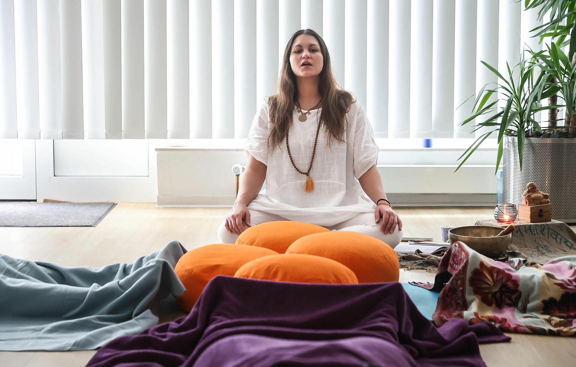 Eine Yogalehrerein sitzt auf einem Meditationskissen und führt Schülerinnen durch eine Yogaübung