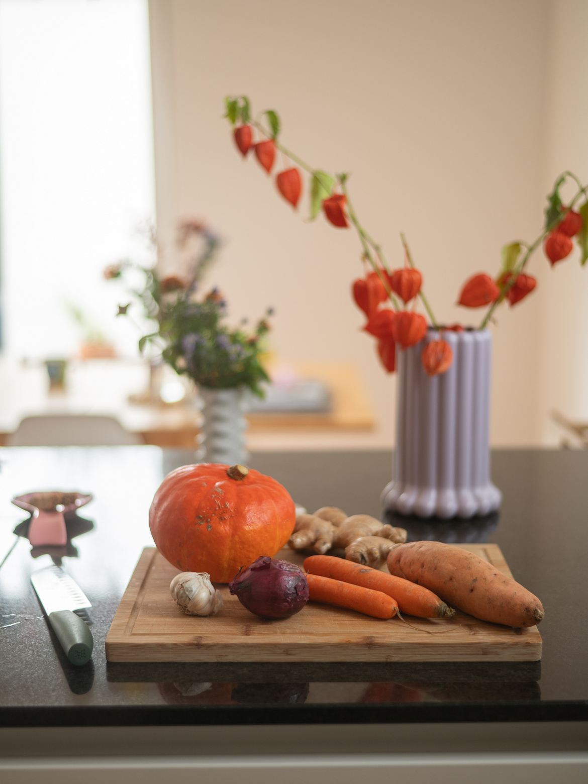 Ein Holzschneidebrett mit Gemüse und eine Blumenvase im Hintergrund