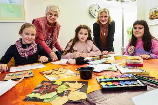 3 Mädchen und 2 Frauen hinter einem Mal- und Basteltisch