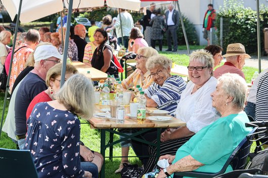 Menschen sitzen an einer Bierzeltgarnitur und unterhalten sich