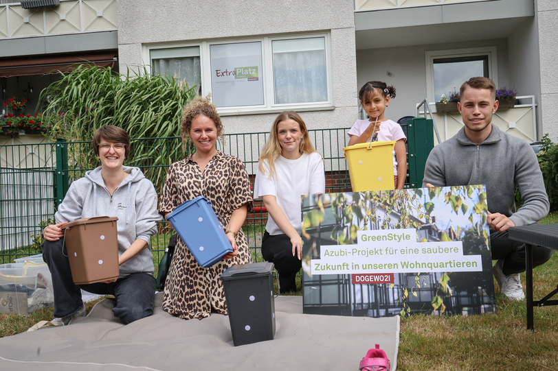 Drei Frauen, ein Mädchen und ein Mann im Garten vom Nachbarschaftstreff halten kleine Müllbehälter in verschiedenen Farben und lächeln in die Kamera.