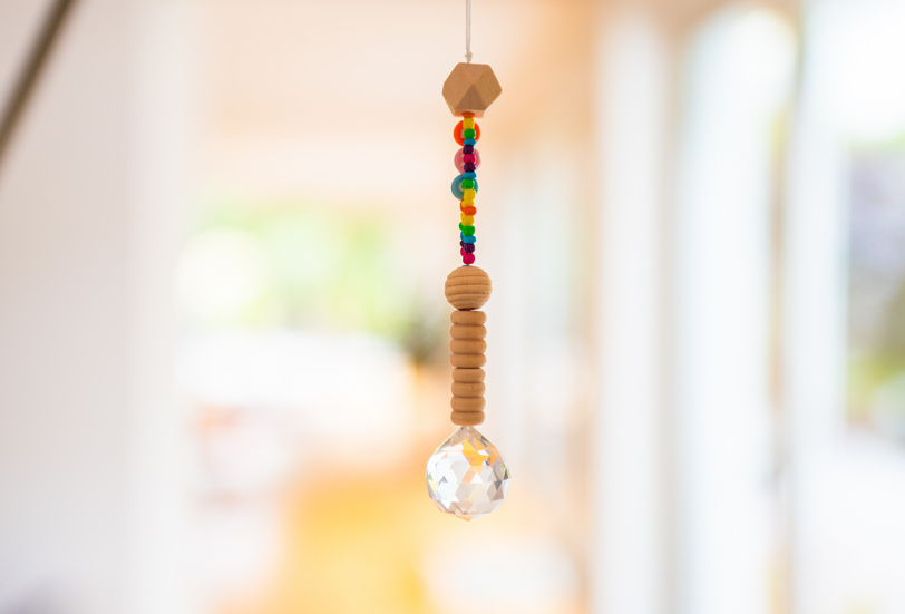 Ein Lichtfänger aus Holz- und Kunststoffkugeln, der im Fenster hängt.