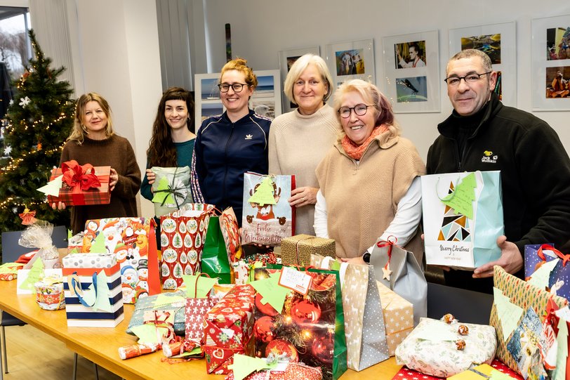 6 Menschen hinter einem Tisch mit Weihnachtsgeschenken