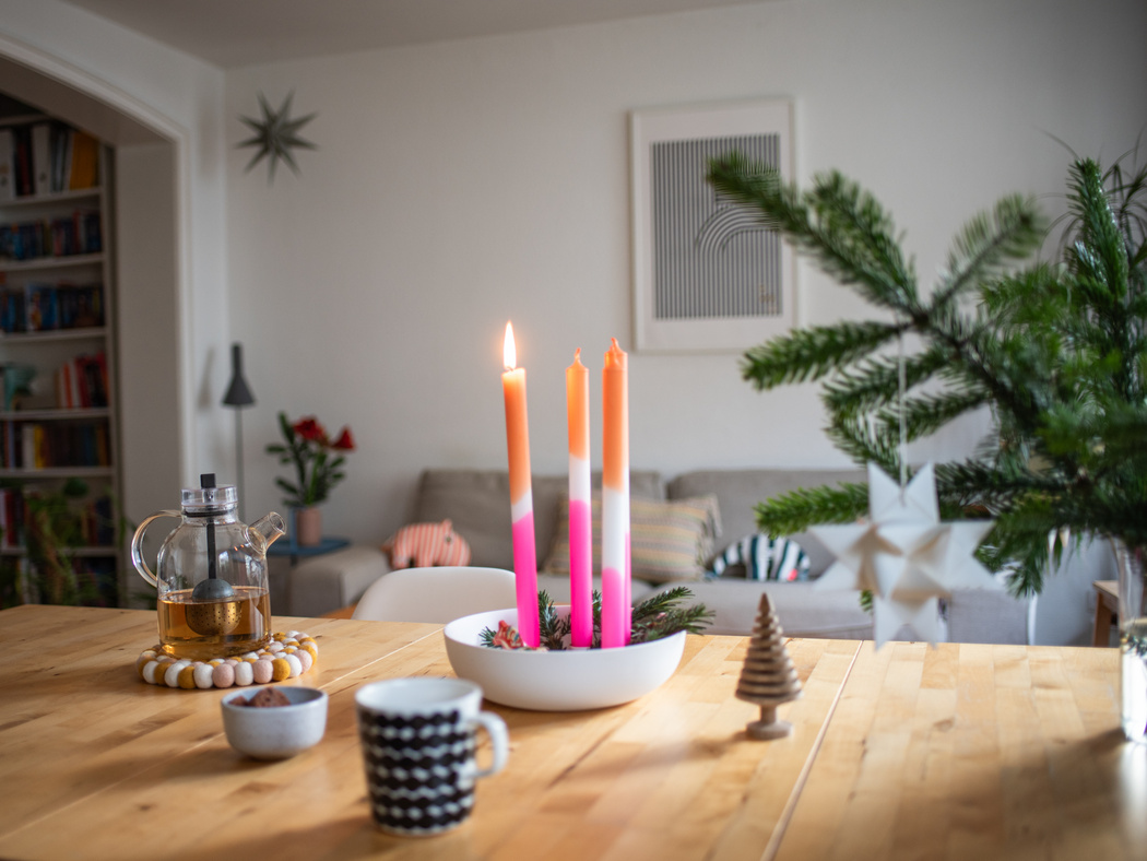 Ein Esstisch mit einem Kerzenhalter mit pink-organgenen Stabkerzen und einer tasse auf dem Tisch