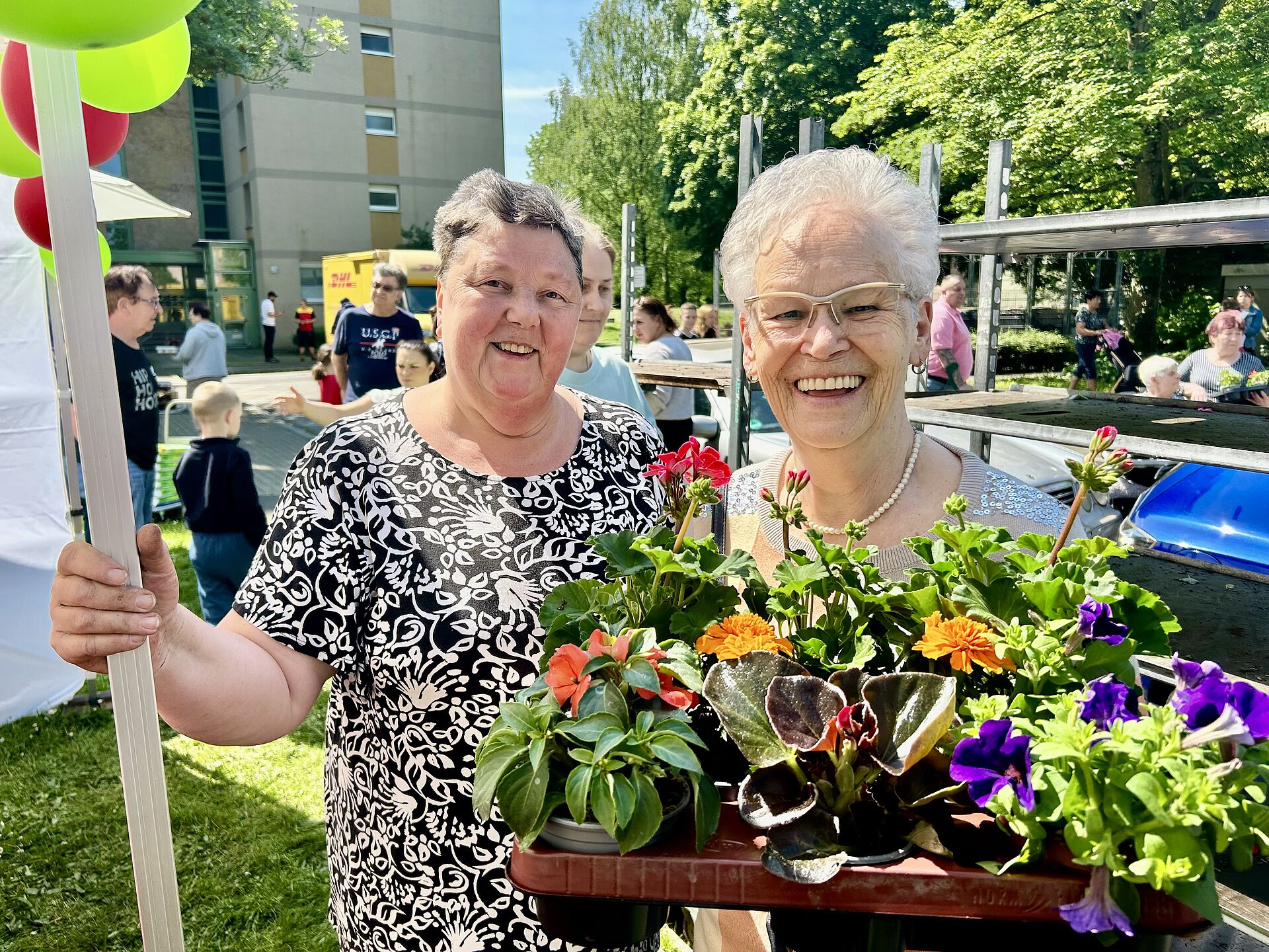 Zwei Frauen blicken lächelnd in die Kamera und freuen sich über ihre Balkonblumen.