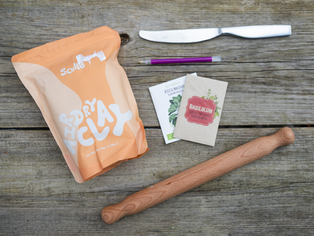 Selbsttrocknender Ton, eine Teigrolle, ein Messer und Kräuter-Tüten auf einem Tisch.