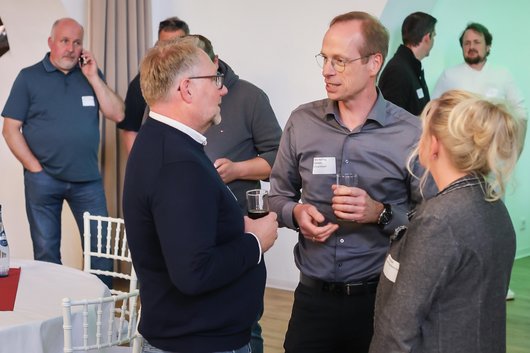 Drei Menschen stehen neben einem Tisch und unterhalten sich interessiert.