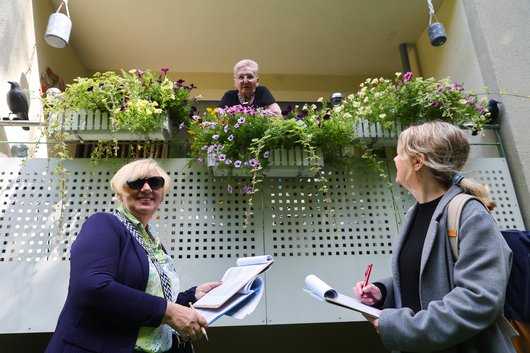 Zwei Jury-Mitglieder sprechen mit einer Mieterin, die ihren Balkon wundervoll bepflanzt hat