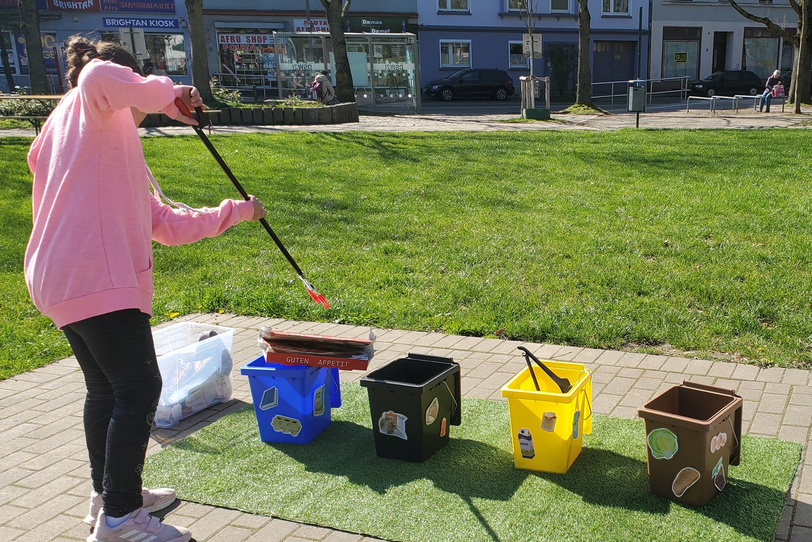 Ein Mädchen sortiert mit einer Greifzange Müll in einen von mehreren Behältern.