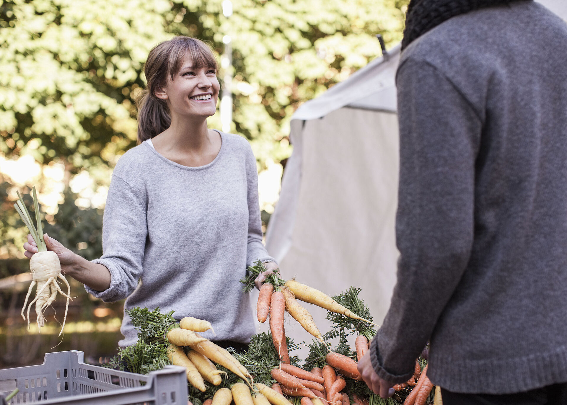 Eine Frau steht lachend hinter einem Gemüsestand auf dem Markt