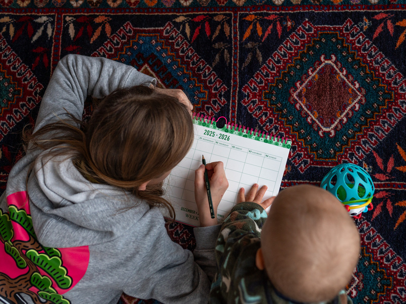 Ein kleines Mädchen schreibt etwas mit einem Bleistift in einen Kalender und ein kleines Baby schaut zu.