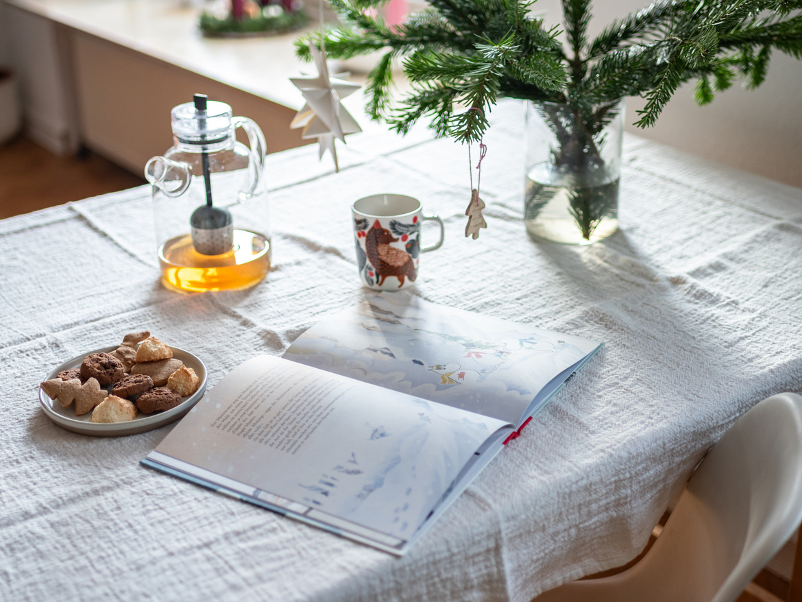 Ein aufgeklapptes Buch auf dem Tisch und daneben eine Tasse Tee.