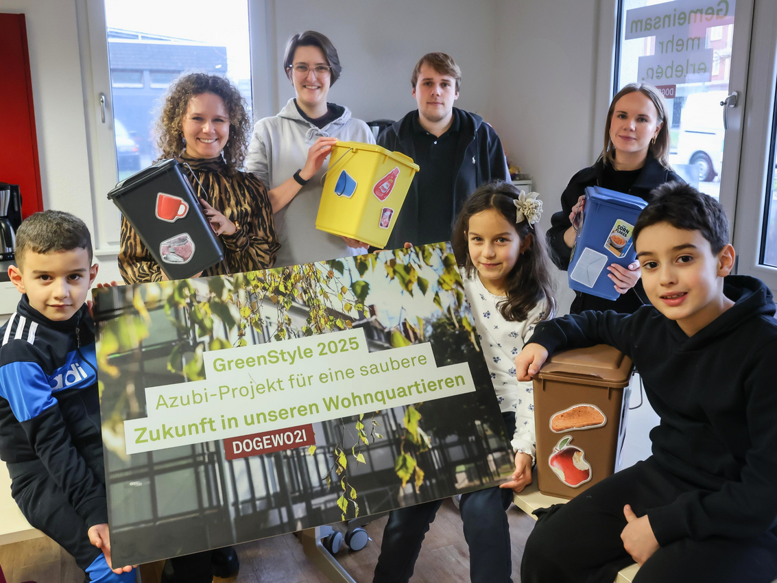 Mehrere Kinder und Erwachsene halten ein Plakat zum Projekt GreenStyle und kleine, bunte Mülleimer in die Kamera.