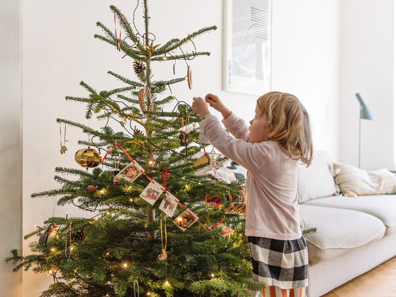 Ein kleines Mädchen schmückt im Wohnzimmer einen Tannenbaum