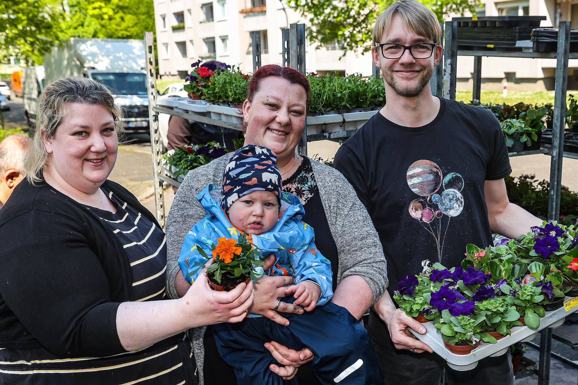 Zwei Frauen mit Baby und ein Mann lächeln mit Blumen in die Kamera